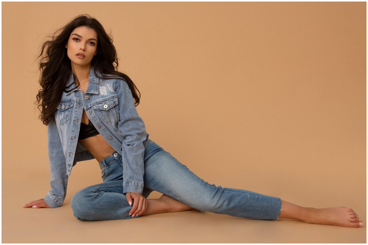 Modelka ubrana w kurtkę i spodnie jeansowe siedzi na podłodze i reklamuje aktualne trendy w modzie